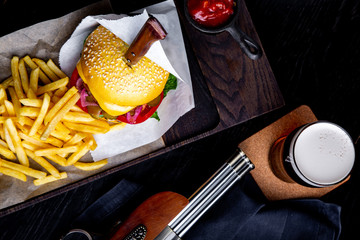 Craft beef burger and french fries on table in restaurant with glass of beer on dark background. Modern fast food lunch frame