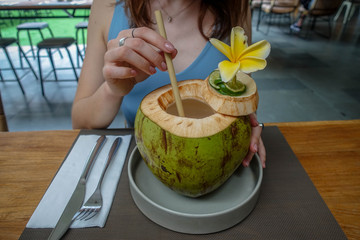 Young woman holding bamboo straw to drink fresh coconut in cafe. Isolated. Bali, Indonesia