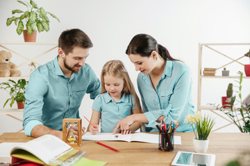 Father, mother and their daughter are smiling while spending time together. A day with family. Young happy couple with child are learning to draw. Education, studying and knowledge sharing concept.
