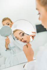 selective focus of attractive woman brushing eyebrows and looking at mirror in bathroom
