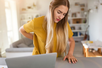 Tired woman suffering backache while using laptop