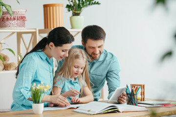Father, mother and their daughter are smiling while spending time together. A day with family. Young happy couple with child are studying with the tablet. Education, studying and knowledge sharing
