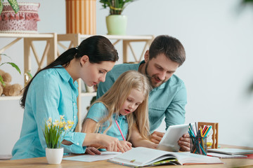 Fototapeta premium Father, mother and their daughter are smiling while spending time together. A day with family. Young happy couple with child are studying with the tablet. Education, studying and knowledge sharing