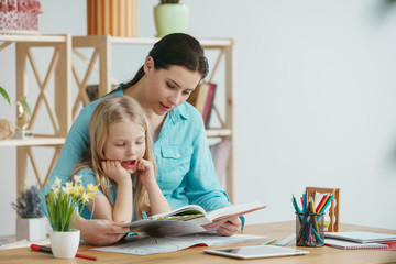 Mother and her daughter spending time together. A day with family. Young pretty girl and her mom are studying with book. Education, studying and knowledge sharing concept.