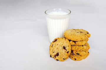 Stack of oats and cranberry wholewheat cookies and a glass of milk on white background. Copy space