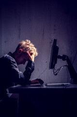 Young Man in front of a Computer Screen resting his Head
