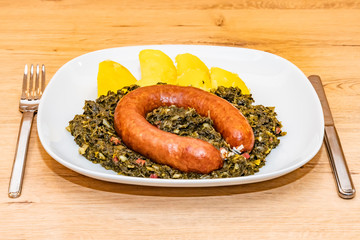 Grünkohl mit Bregenwurst und Kartoffeln auf weißen Teller mit Besteck