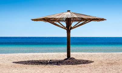 one wooden beach umbrella on the sand on the beach against the blue water of the Red Sea in Egypt Dahab South Sinai