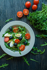 Greek salad with fresh tomatoes, arugula, eggs, olives with olive oil on a dark wood background. Healthy food. Veggie dish.