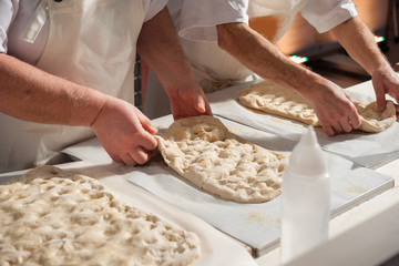 The baker is preparing a focaccia dough on a countertop.