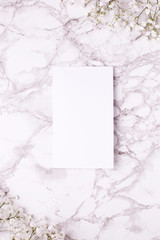 Empty card with white flowers on marble table top view and flat lay style.