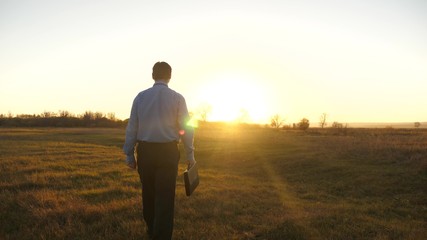 Business man with briefcase goes on beautiful sunset after working day.