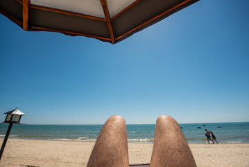 Beach wooden straw sunshade umbrella. Male feet on the sea with sand beach