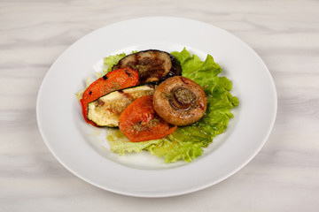 Fried mushroom champignon, eggplant, tomato and green leaf lettuce on a white round plate.