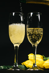 Elegant glasses of yellow champagne and yellow tulips on black background
