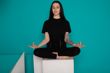 Beautiful young  woman sitting in yoga position and meditating isolated over blue background  - obrazy, fototapety, plakaty