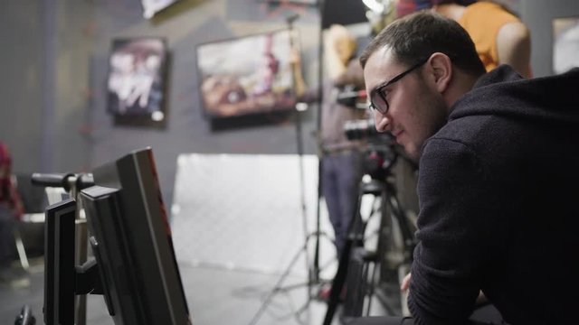 Male director with glasses is watching the monitor while directing a movie shooting