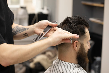 Handsome bearded man, having hair cut by scissors at barber shop .