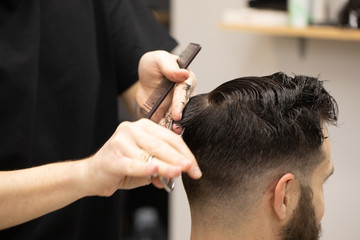 Handsome bearded man, having hair cut by scissors at barber shop .