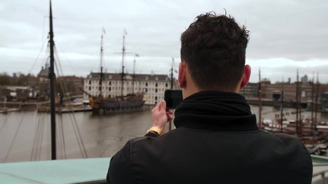 SLOW MOTION: Male tourist is taking pictures of an old ship in Amsterdam with his mobile phone