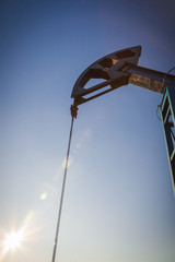Oil pump on the background of blue sky and the morning sun, sun glare on the oil pump