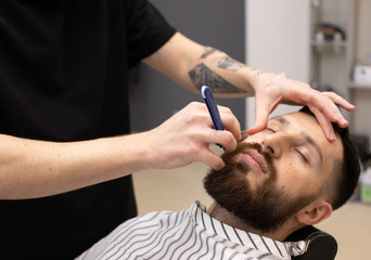 Shaving process of beards in Barbershop. Master makes a haircut beard client with vintage straight...
