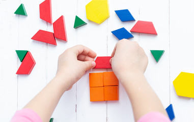 A child plays with colored blocks constructs a model on a light wooden background - 256485603