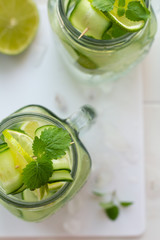 glasses with water, mint, lime and cucumber on a white board. top view close-up.