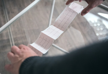 The patient's hands are holding a medical cardiogram printed on paper