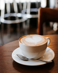 One cup of cappuccino with latte art on wooden table, white ceramic cup, place for text. Cafe culture.