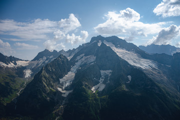 The peaks of the Caucasus Mountains in cloudy clouds and the rays of the sun through them in the outskirts of Dombai. And on the tops of snow lies.