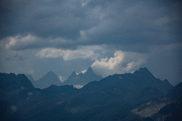 Fototapeta premium The peaks of the Caucasus Mountains in cloudy clouds and the rays of the sun through them in the outskirts of Dombai. And on the tops of snow lies.