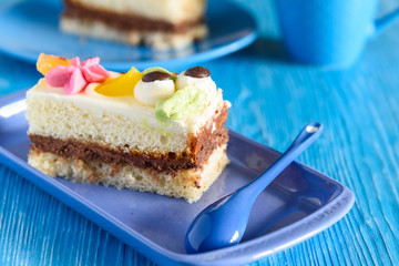 Puff biscuit cake with custard on a ceramic plate, behind the cup of coffee, photographed on a blue wooden background.