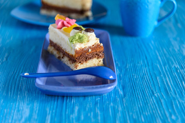 Puff biscuit cake with custard on a ceramic plate, behind the cup of coffee, photographed on a blue wooden background.