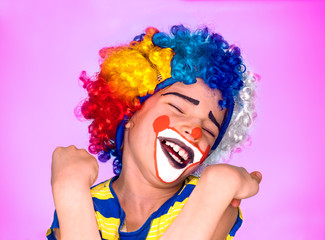 Funny child clown wig enjoying a good joke having a hearty laugh with mouth open and eyes closed as he deviates from the camera.