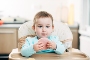 Fototapeta premium a little girl in a high chair with a piece of boiled sausage in her hands