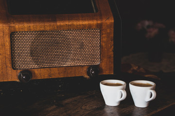 Two coffee cups with espresso and retro radio on dark wooden background. Vintage color tone