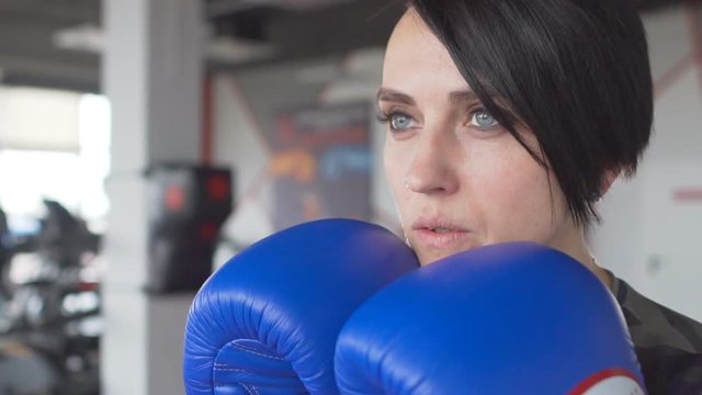 Close up portrait of a serious female boxer with gloves inside a boxing ring. Woman with short hair style in gym
