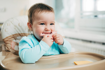 a little girl in a high chair eating a piece of boiled sausage