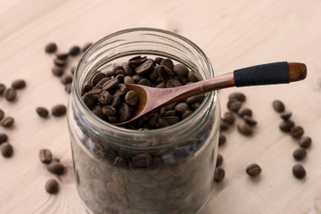 Roasted coffee beans in a glass jar with wooden spoon