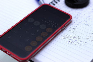 Phone calculator, notebook with calculations written by hand.