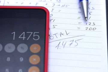 Phone calculator, notebook with calculations written by hand.