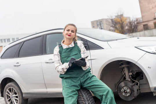 Woman mechanic in uniform posing on spare wheel