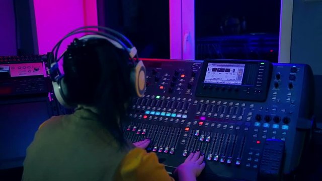 Woman DJ works at the mixing console in color lighting