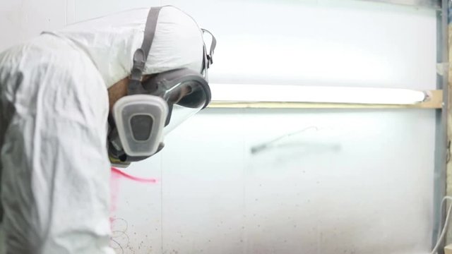 profession, people, carpentry, emotion and people concept -Man paints skateboard in workshop, applies varnish. manufacture of skateboards. he has protective clothing and mask. 4k