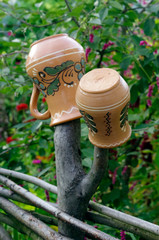 Сeramic pots hang on a wicker fence against a background of flowering bushes