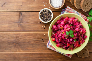 Traditional russian salad vinaigrette with boiled vegetables, pickled cucumbers and sauerkraut in bowl on wooden table. Top view. Copy space.