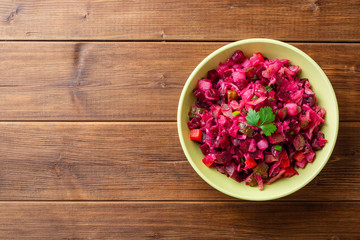 Traditional russian salad vinaigrette with boiled vegetables, pickled cucumbers and sauerkraut in bowl on wooden table. Top view. Copy space.