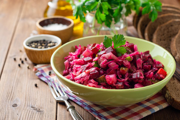 Traditional russian salad vinaigrette with boiled vegetables, pickled cucumbers and sauerkraut in bowl on wooden table. Selective focus.