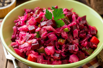 Traditional russian salad vinaigrette with boiled vegetables, pickled cucumbers and sauerkraut in bowl on wooden table. Selective focus.